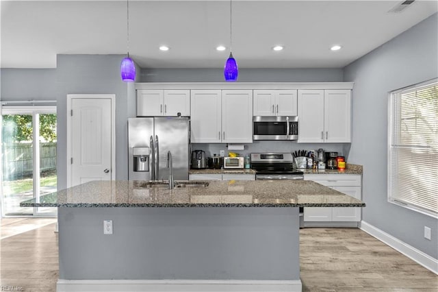 kitchen featuring light wood-type flooring, white cabinetry, a center island with sink, stainless steel appliances, and a sink