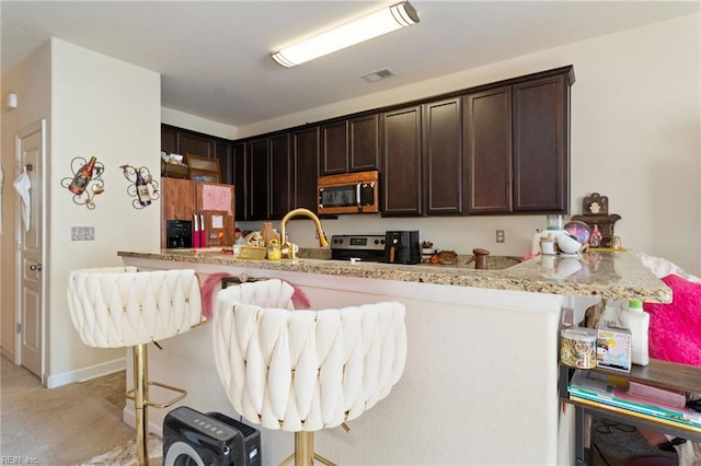 kitchen featuring a breakfast bar area, light colored carpet, dark brown cabinets, and stainless steel appliances