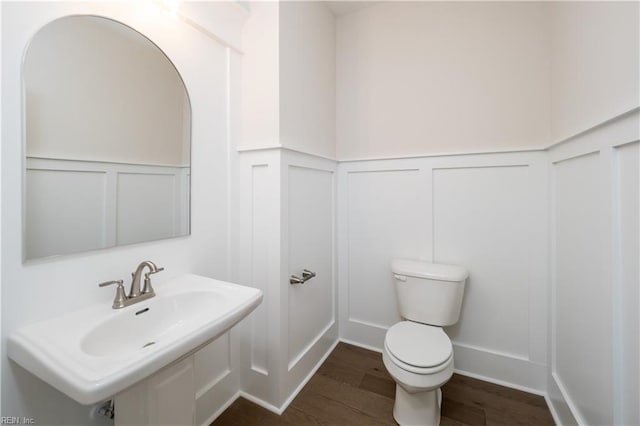 half bath featuring a decorative wall, toilet, and wood finished floors