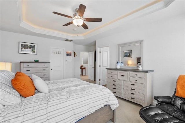 bedroom with a raised ceiling, visible vents, light colored carpet, and ceiling fan