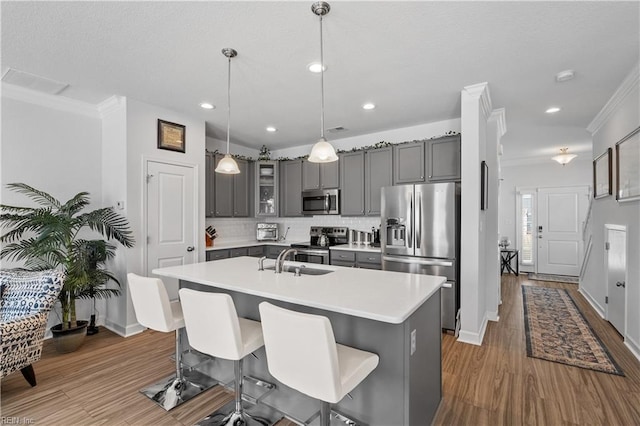 kitchen featuring a sink, backsplash, gray cabinetry, appliances with stainless steel finishes, and ornamental molding