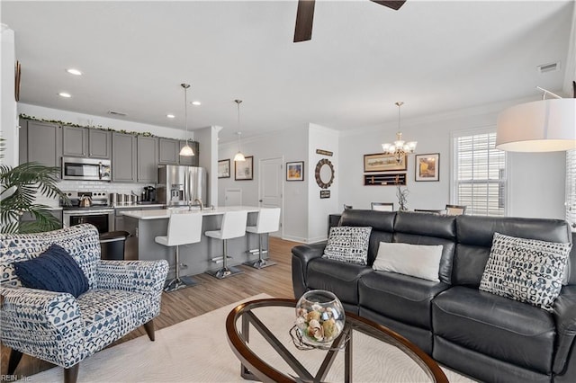 living room with light wood-style flooring, visible vents, recessed lighting, ceiling fan with notable chandelier, and ornamental molding