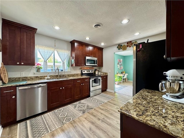 kitchen with light wood-type flooring, a textured ceiling, appliances with stainless steel finishes, and a sink