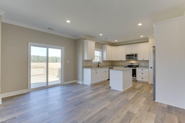kitchen featuring baseboards, crown molding, a kitchen island, stainless steel appliances, and a sink