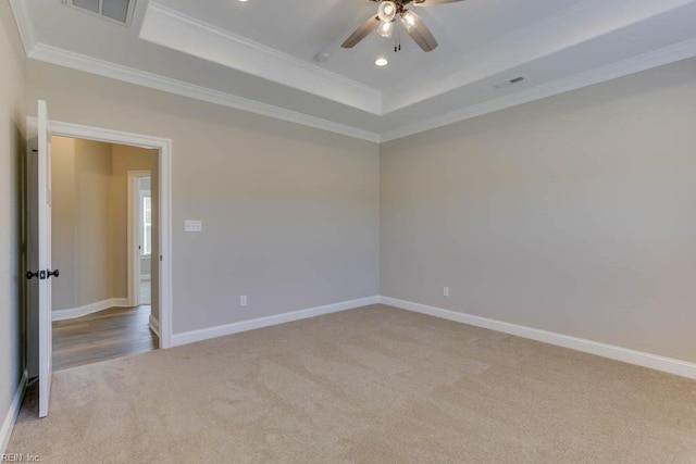carpeted spare room featuring a raised ceiling, ceiling fan, ornamental molding, and visible vents