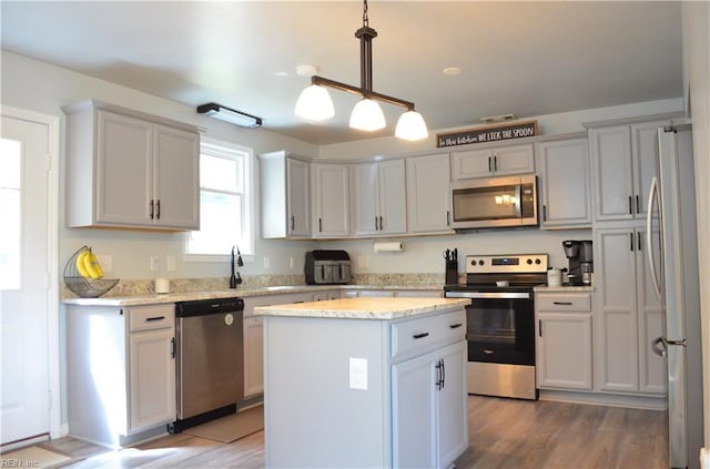 kitchen featuring a center island, decorative light fixtures, a sink, appliances with stainless steel finishes, and wood finished floors