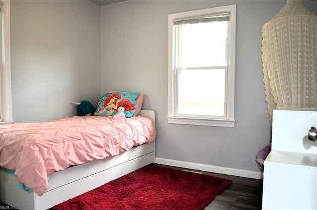bedroom with multiple windows, baseboards, and wood finished floors