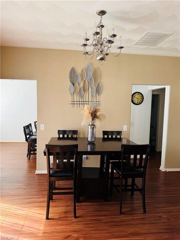 dining space with visible vents, baseboards, wood finished floors, and a chandelier
