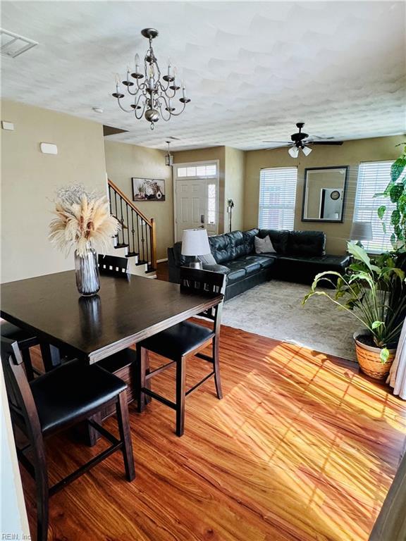 dining space with ceiling fan with notable chandelier, wood finished floors, and stairway
