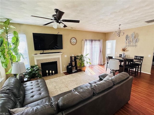 living area with a fireplace with flush hearth, wood finished floors, visible vents, baseboards, and ceiling fan with notable chandelier