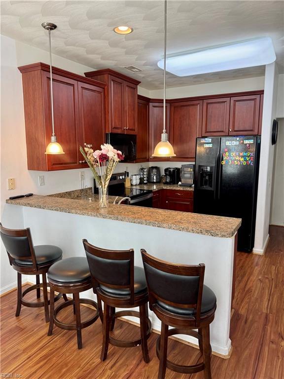 kitchen featuring light wood finished floors, a breakfast bar, pendant lighting, black appliances, and a peninsula