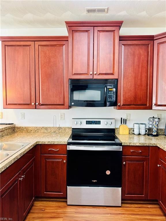kitchen featuring stainless steel electric stove, black microwave, dark brown cabinets, and light wood-type flooring