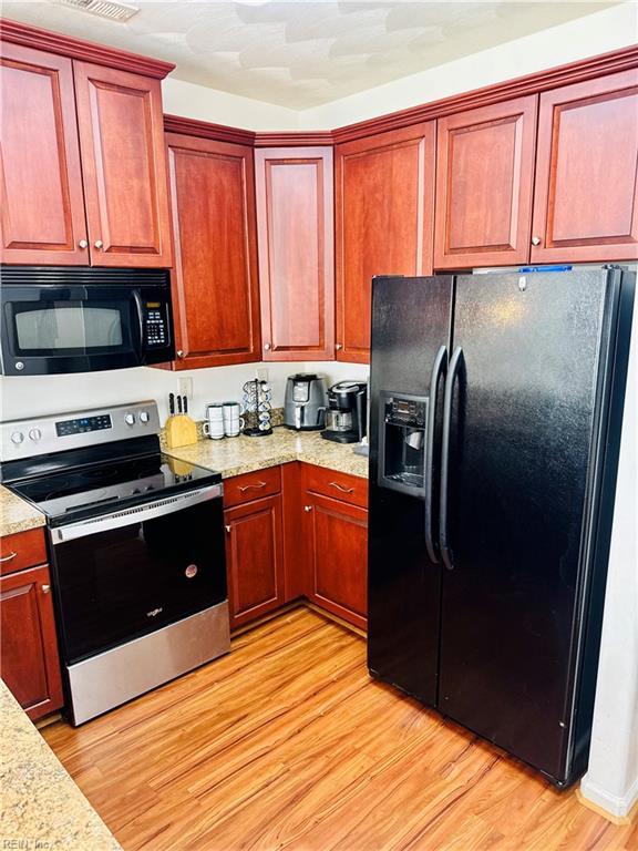 kitchen featuring light wood-style floors, light stone countertops, dark brown cabinets, and black appliances