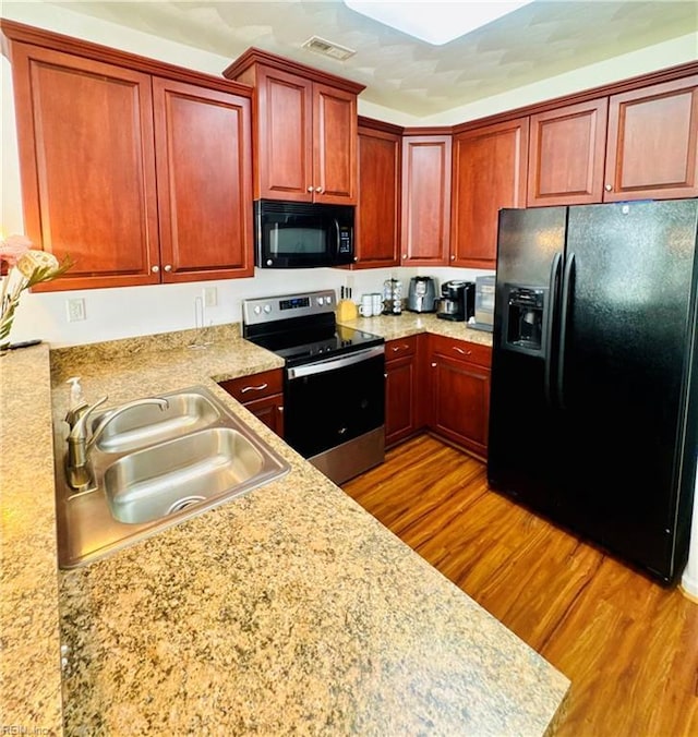 kitchen featuring a sink, visible vents, wood finished floors, light countertops, and black appliances