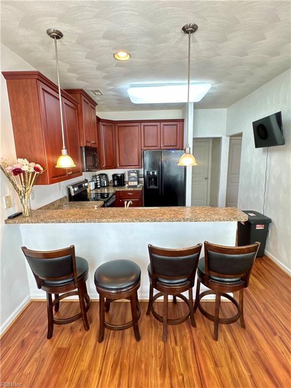 kitchen featuring black appliances, baseboards, light wood-style flooring, decorative light fixtures, and a peninsula