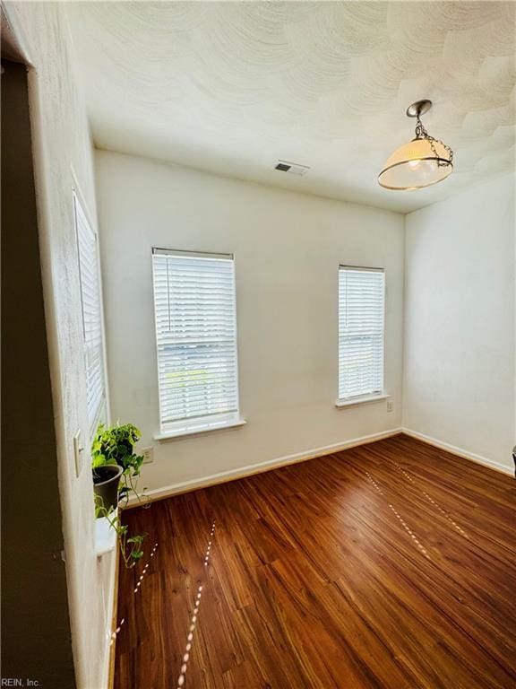 empty room with wood finished floors, visible vents, and baseboards