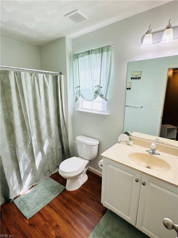bathroom featuring wood finished floors, visible vents, toilet, vanity, and a shower with curtain