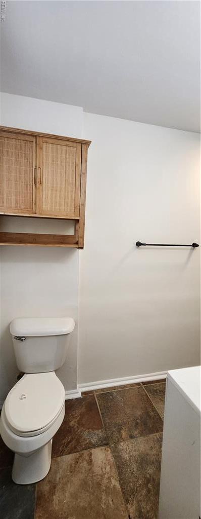 bathroom with toilet, baseboards, and stone finish flooring