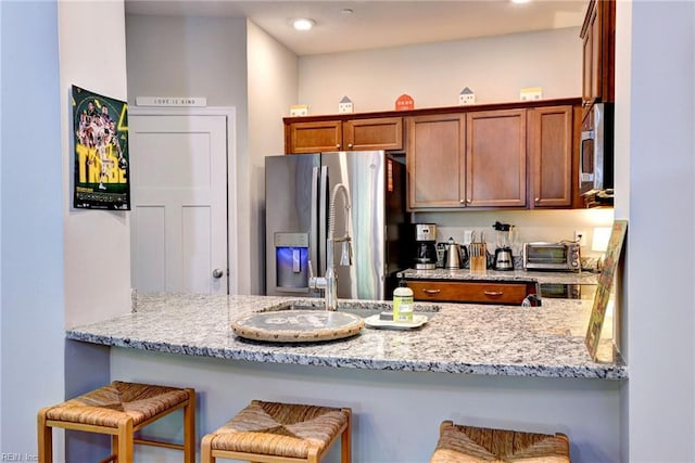 1208 Kings Land Ct, Williamsburg, VA 23185 - kitchen featuring a peninsula, brown cabinetry, light stone counters, and stainless steel appliances