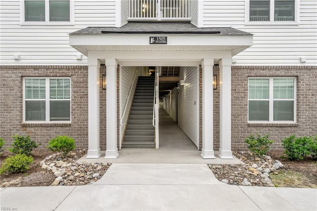 entrance to property featuring brick siding and roof with shingles