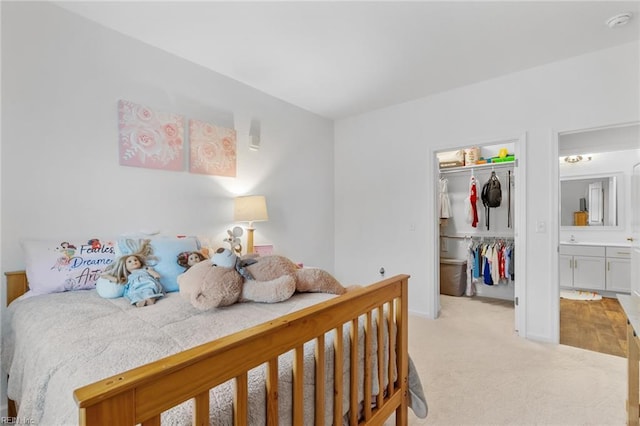 bedroom with a walk in closet, a closet, baseboards, and light carpet