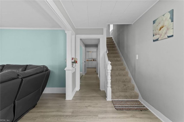 staircase featuring ornate columns, baseboards, ornamental molding, and wood finished floors