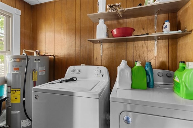 laundry room featuring electric water heater, wooden walls, washer and clothes dryer, and laundry area