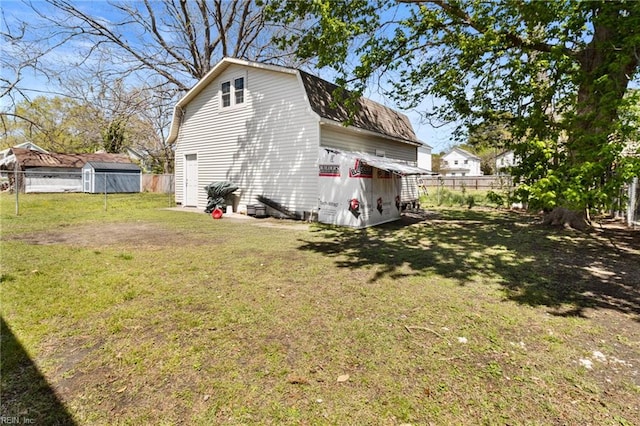 exterior space with roof with shingles, a gambrel roof, fence, and a lawn
