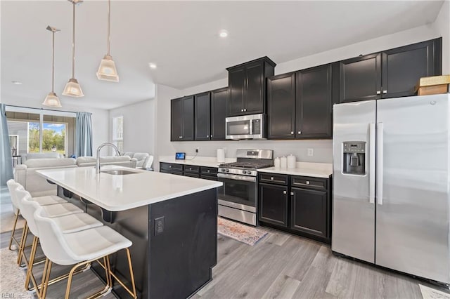 kitchen featuring open floor plan, light countertops, stainless steel appliances, light wood finished floors, and a sink