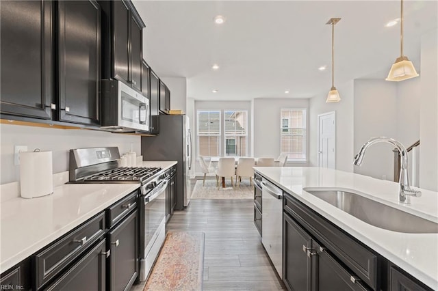 kitchen featuring decorative light fixtures, dark cabinetry, dark wood finished floors, stainless steel appliances, and a sink