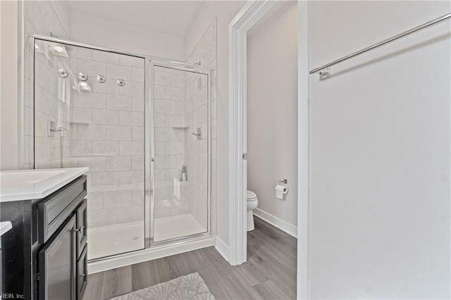 bathroom with baseboards, toilet, vanity, wood finished floors, and a stall shower