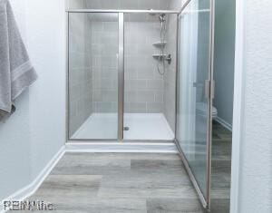full bathroom with toilet, baseboards, a stall shower, and wood finished floors