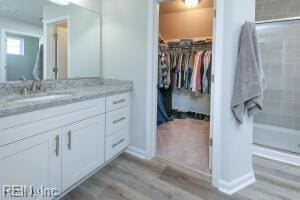 full bath featuring a shower stall, wood finished floors, vanity, and a walk in closet