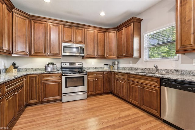 kitchen featuring recessed lighting, light stone counters, a sink, light wood-style floors, and appliances with stainless steel finishes