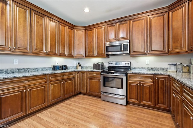 kitchen with brown cabinets, appliances with stainless steel finishes, light stone countertops, and light wood-style floors