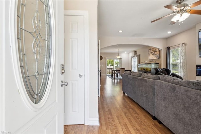 entryway with arched walkways, light wood-type flooring, ceiling fan, and plenty of natural light