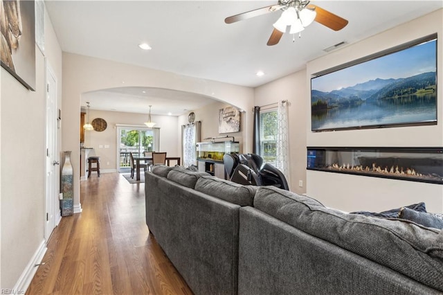 living area featuring wood finished floors, ceiling fan, arched walkways, baseboards, and recessed lighting