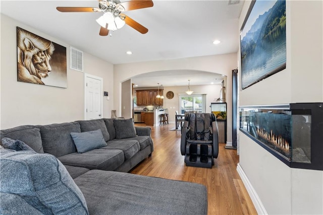 living room featuring arched walkways, light wood-type flooring, visible vents, recessed lighting, and a ceiling fan