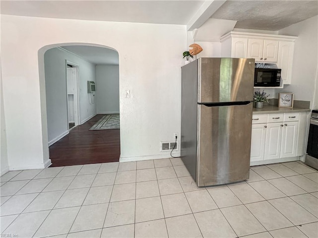 kitchen featuring white cabinets, arched walkways, visible vents, freestanding refrigerator, and black microwave