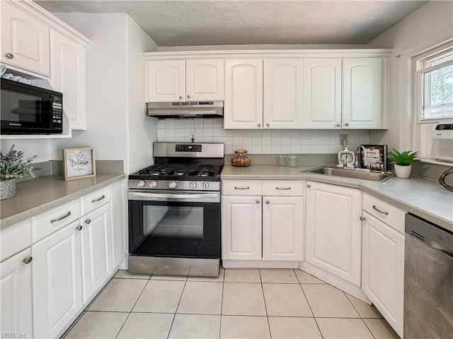 kitchen featuring white cabinets, a sink, appliances with stainless steel finishes, under cabinet range hood, and light tile patterned floors