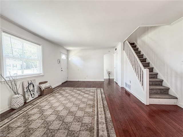 unfurnished living room featuring stairway, hardwood / wood-style flooring, arched walkways, baseboards, and visible vents