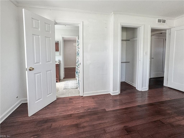 unfurnished bedroom featuring baseboards, crown molding, wood finished floors, and visible vents