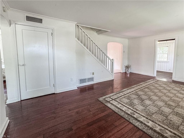unfurnished living room featuring stairway, wood finished floors, visible vents, arched walkways, and crown molding