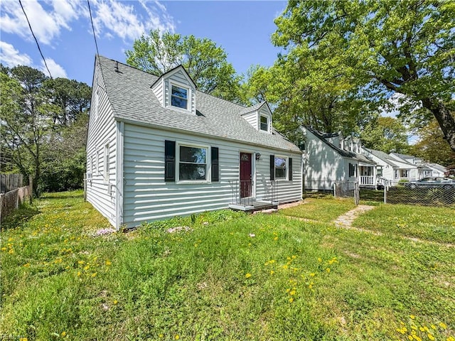 cape cod-style house with roof with shingles, a front yard, and fence