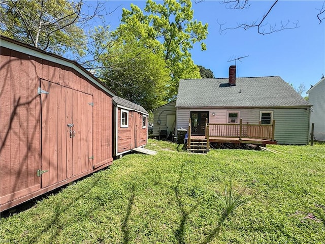 rear view of house with a lawn, an outdoor structure, a chimney, and a deck