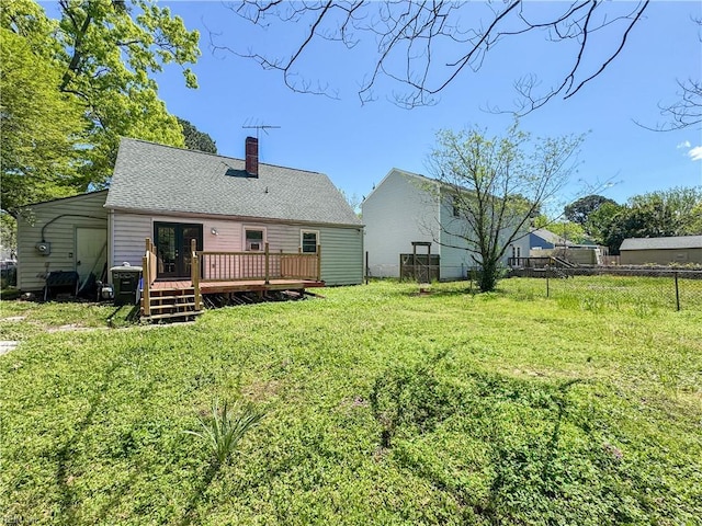 rear view of property featuring a chimney, a lawn, fence, a wooden deck, and roof with shingles