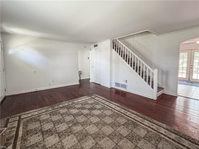 unfurnished living room with hardwood / wood-style flooring, arched walkways, stairway, and crown molding
