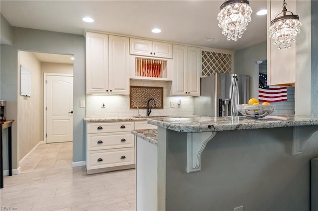 kitchen featuring decorative backsplash, stainless steel refrigerator with ice dispenser, light stone counters, and a sink