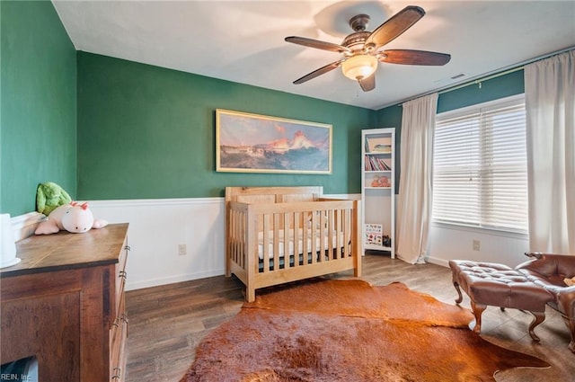 bedroom with a ceiling fan, wood finished floors, a wainscoted wall, baseboards, and visible vents