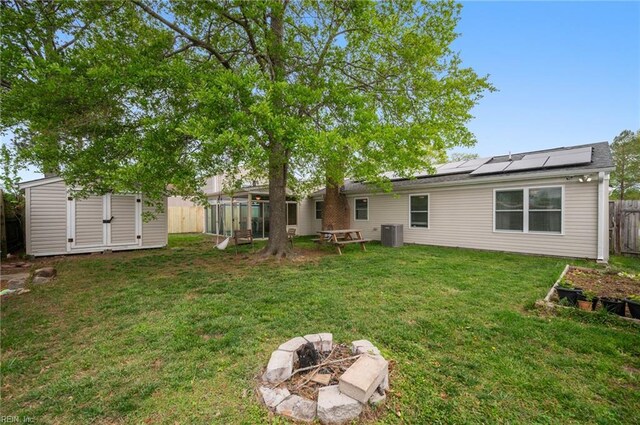 back of property with a fenced backyard, a fire pit, an outdoor structure, roof mounted solar panels, and a shed